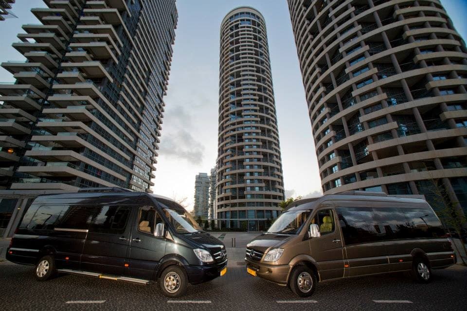 Two Mercedes-Benz Sprinter vans with a modern city skyline at golden hour
